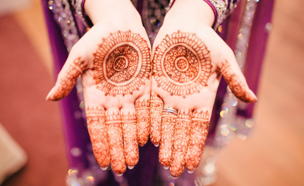 A pair of hands held palms out, tattooed with henna ink in an intricate pattern