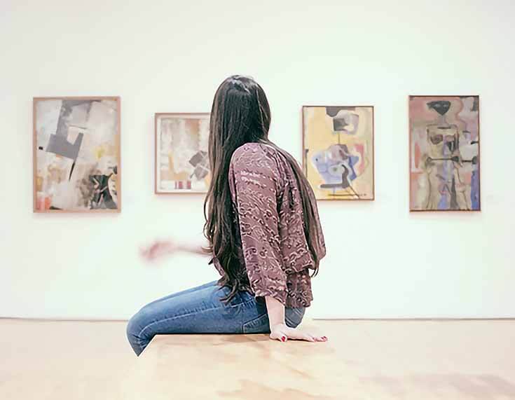 Photo of a woman looking at several pieces of art on the wall