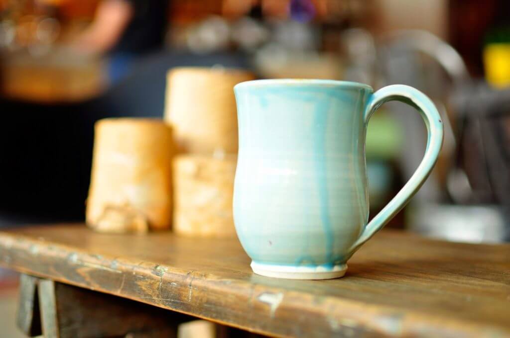 Handmade ceramic mug painted in light blue on a potter's table