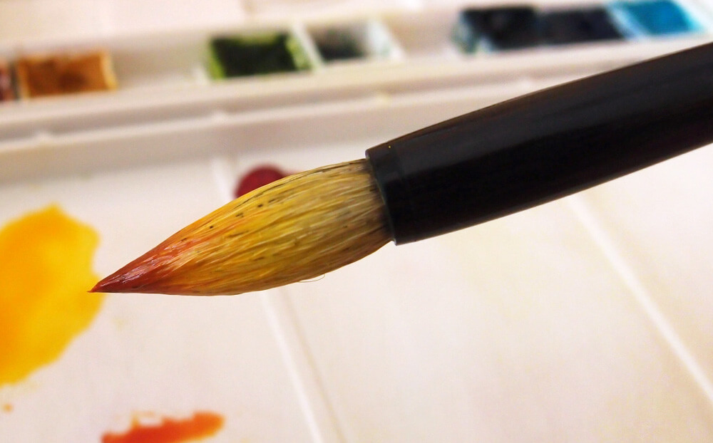 Chinese brush loaded with red and yellow watercolor paint