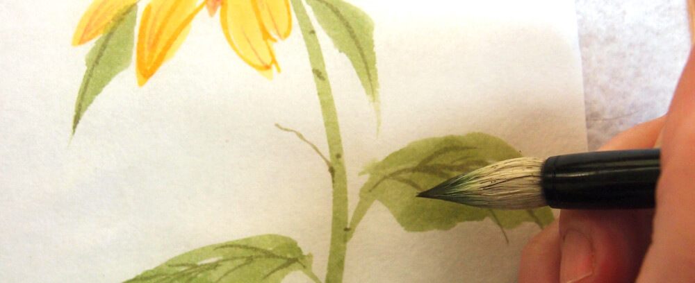 Close-up image of an artist adding veins to a sunflower leaf with a Chinese brush