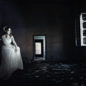Photo illustration of a sitting woman with a wind-up knob in her back. She's in a dark room with a glowing window.
