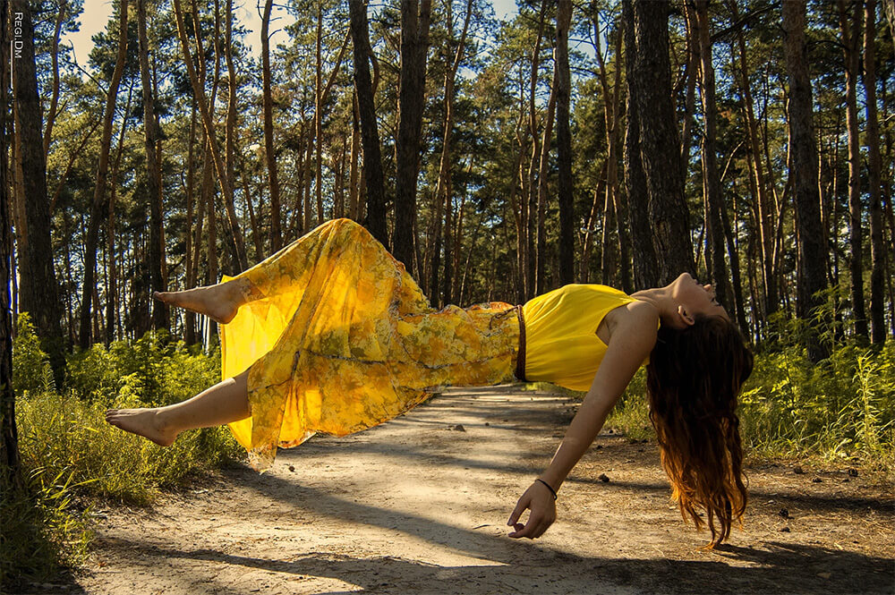 Photo illustration of a woman in a yellow dress floating in mid-air in a sunlit forest