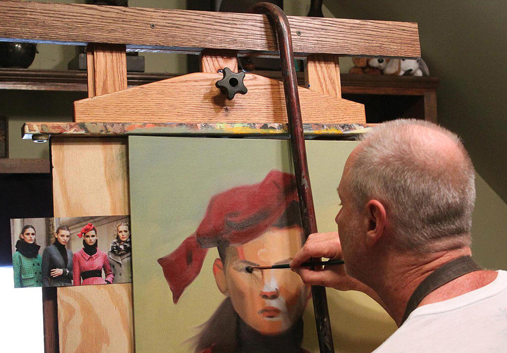 The artist holding a hooked cane over the top of his easel and using it as a straight-edge when painting