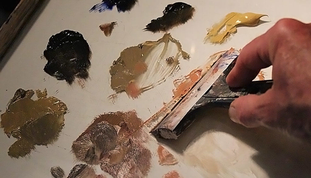 Artist scraping dried oil paint from a clear glass painting palette