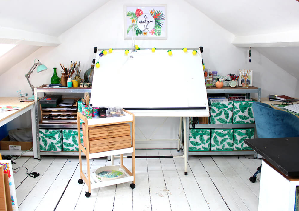 Clean white attic studio space with rolling cart, drafting table, lamps, and storage cubbies